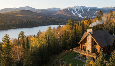 Chalet en bois rond au bord d'un lac avec vue sur les montagnes de ski, illustrant une résidence secondaire à vendre proche de Québec (secteur Stoneham/Lac-Beauport).