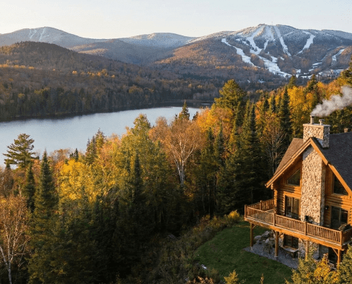 Chalet en bois rond au bord d'un lac avec vue sur les montagnes de ski, illustrant une résidence secondaire à vendre proche de Québec (secteur Stoneham/Lac-Beauport).