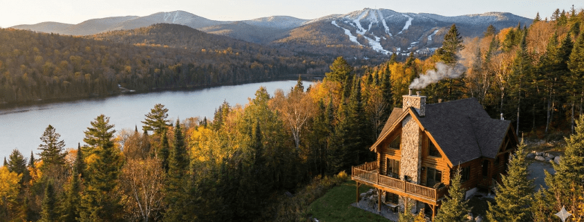 Chalet en bois rond au bord d'un lac avec vue sur les montagnes de ski, illustrant une résidence secondaire à vendre proche de Québec (secteur Stoneham/Lac-Beauport).